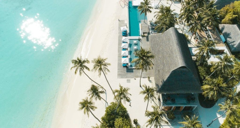 A stunning aerial view of a tropical beach resort with palm trees, turquoise waters, and white sand.