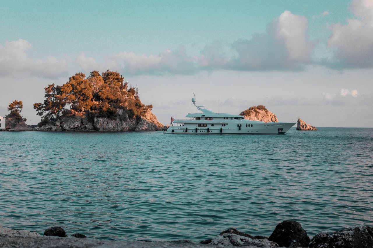 Elegant yacht cruising near a picturesque island with calm turquoise waters and lush greenery.